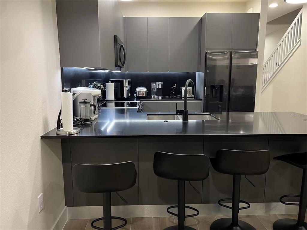 A modern kitchen features dark gray cabinetry, black countertops, and a breakfast bar with stools — 17240 BLESSING DRIVE, CLERMONT, FL