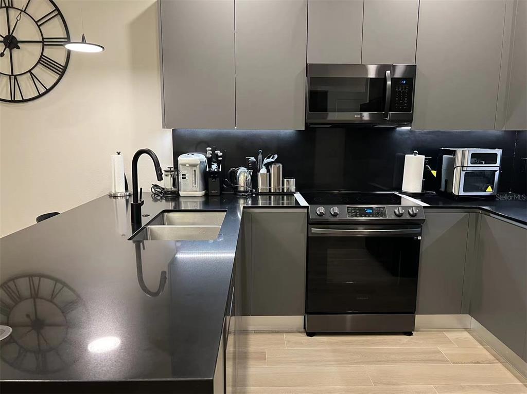 A modern kitchen features gray cabinets, black countertops, stainless steel appliances, and a large wall clock — 17240 BLESSING DRIVE, CLERMONT, FL