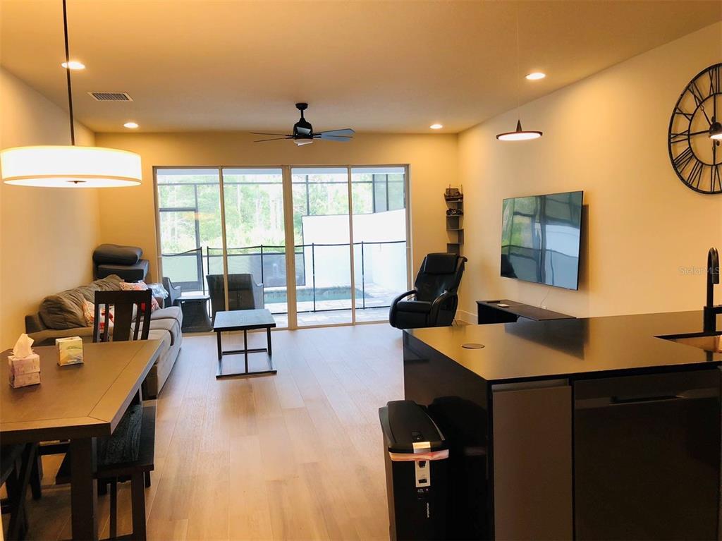 An open-concept living and dining area features light wood floors, a kitchen island, and sliding doors — 17240 BLESSING DRIVE, CLERMONT, FL