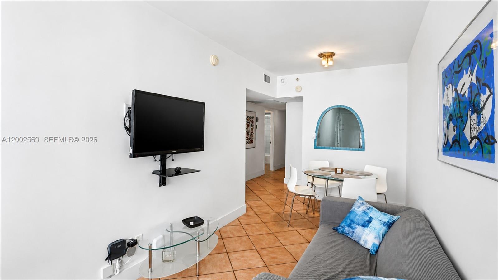 A living room features a wall-mounted television, a glass coffee table, and a dining area — 100 Lincoln Rd # 1209, Miami Beach FL 33139, MIAMI BEACH, FL