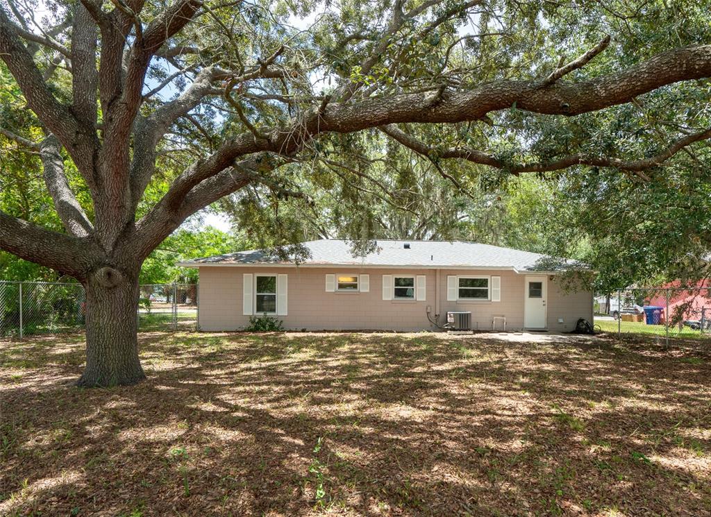 The exterior of a single-story house with tan siding sits behind a large oak tree — 1049 BIRCH BOULEVARD, TAVARES, FL