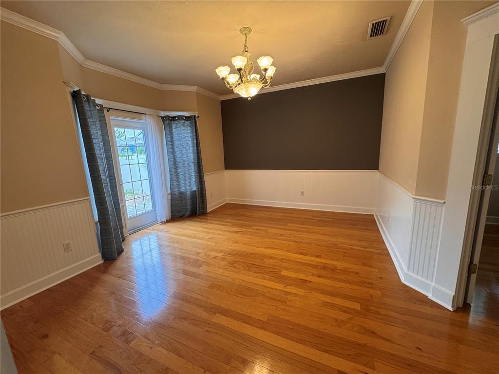 A dining room features hardwood floors, white wainscoting, a dark accent wall, and a chandelier — 5020 NW 10TH PLACE, GAINESVILLE, FL