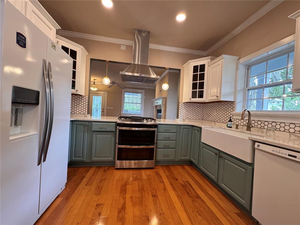 A kitchen features white upper cabinets, sage green lower cabinets, stainless appliances, and hardwood floors — 5020 NW 10TH PLACE, GAINESVILLE, FL