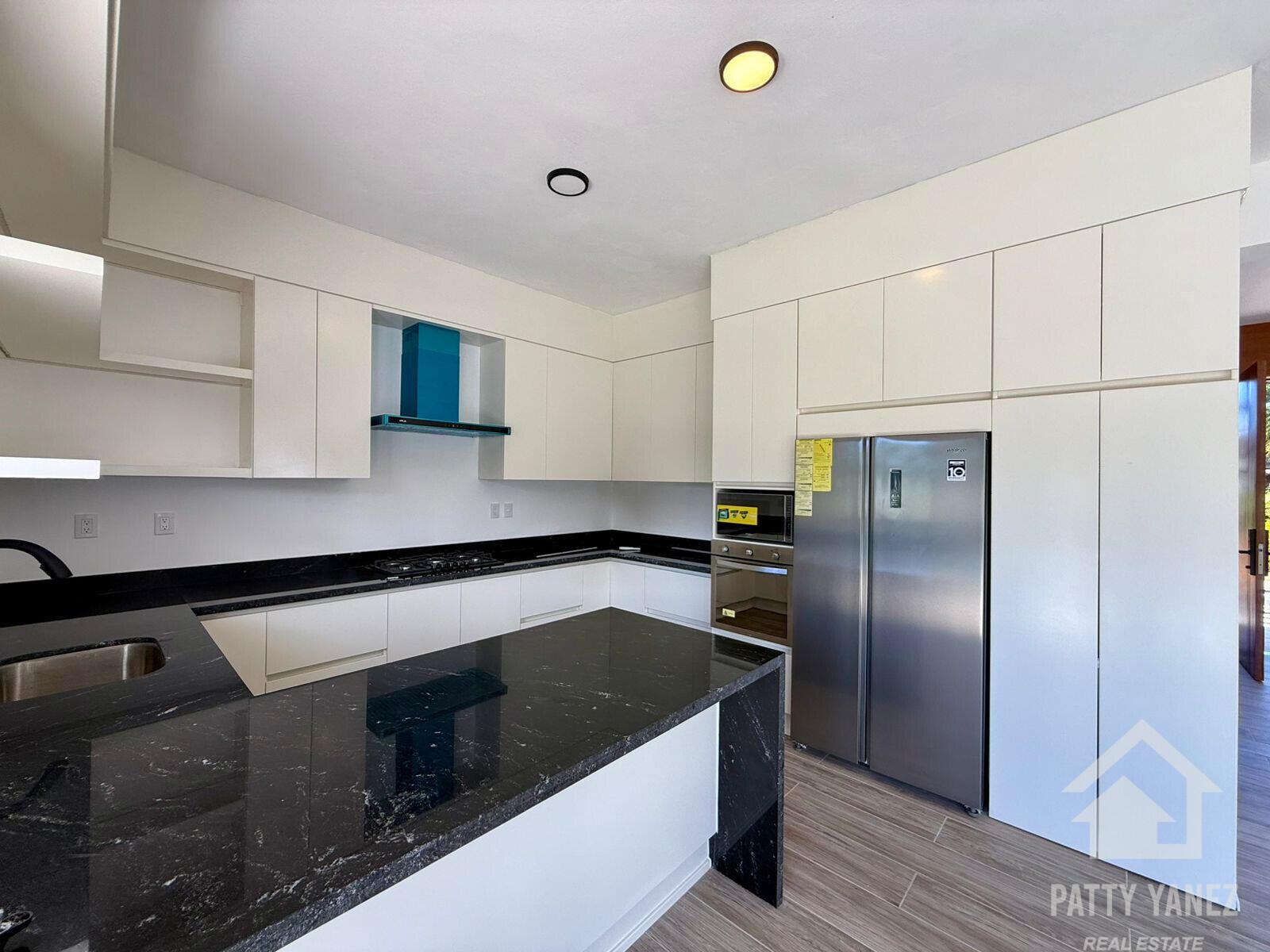 A modern kitchen features white cabinetry, black granite countertops, and stainless steel appliances — Perla Marina Residential Calle Perla, FL