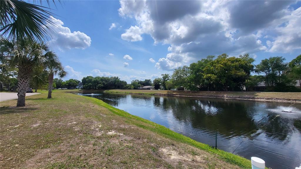 A grassy bank slopes down to a pond with fountains under a cloudy sky — 2291 AMERICUS BOULEVARD W UNIT 37, CLEARWATER, FL