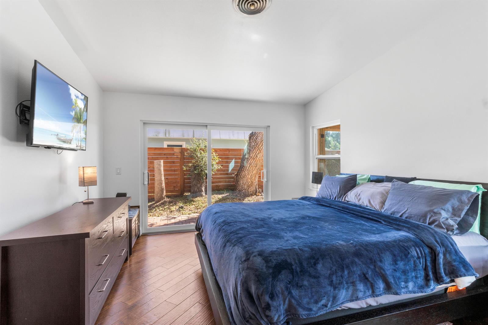 A bedroom with a dark wood dresser, a bed with blue bedding, and sliding glass doors — 616 Dahlia Lane, Vero Beach FL 32963, VERO BEACH, FL