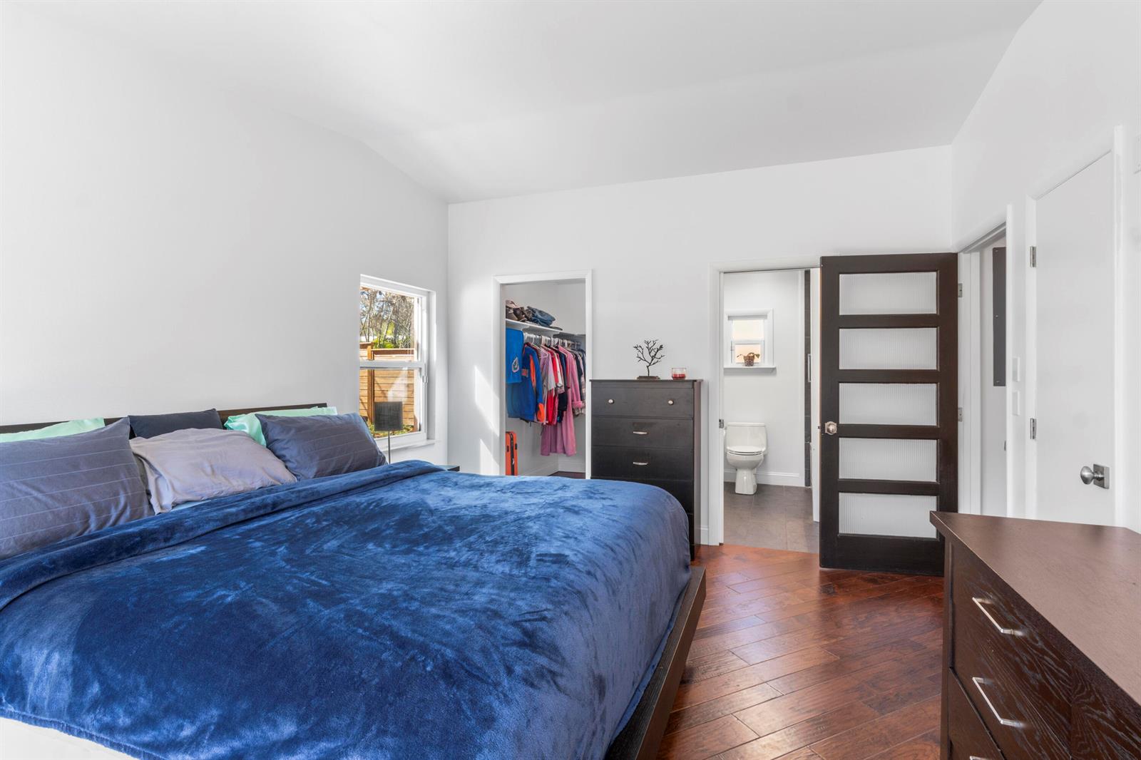 A bedroom with a blue bed, dark wood floors, a walk-in closet, and an ensuite bathroom — 616 Dahlia Lane, Vero Beach FL 32963, VERO BEACH, FL