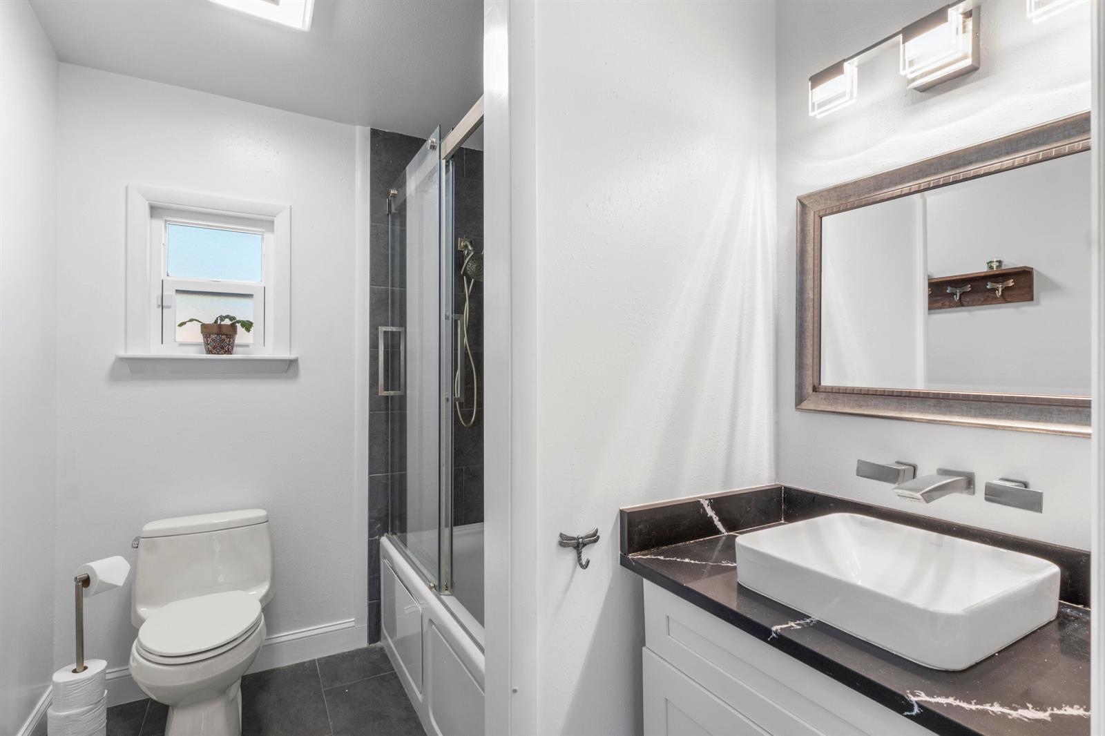 A bathroom features a white vessel sink on a black marble vanity, toilet, and shower — 616 Dahlia Lane, Vero Beach FL 32963, VERO BEACH, FL