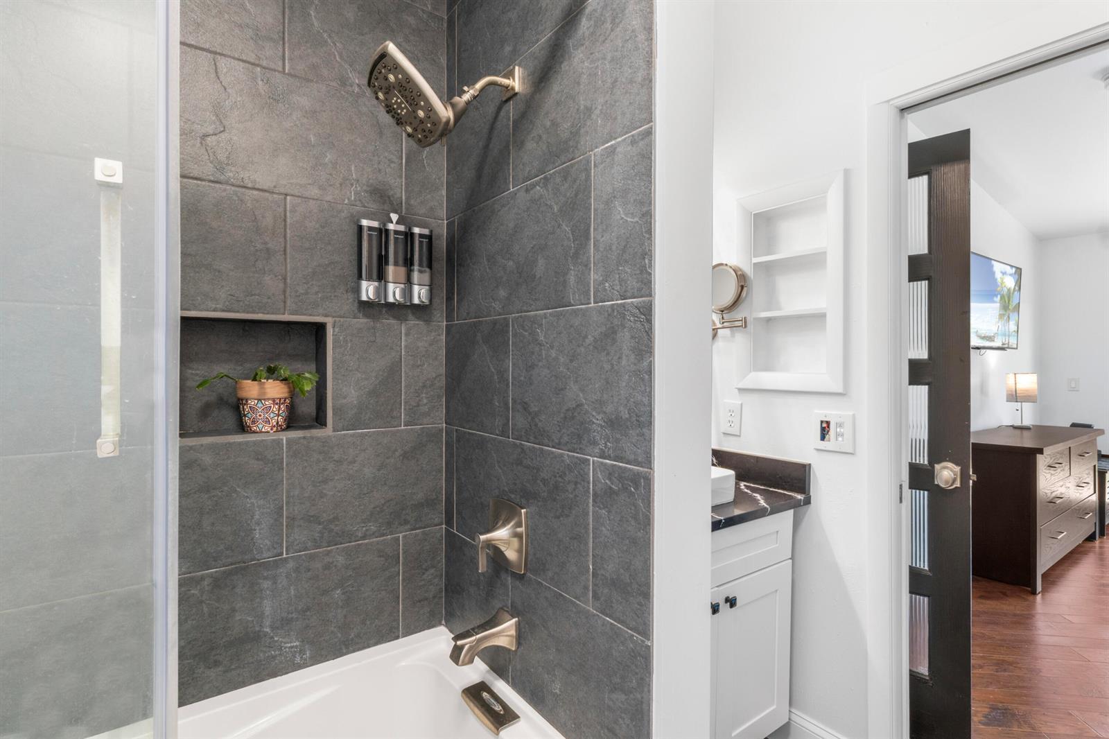 A bathroom features a dark tiled shower with a tub, wall-mounted dispensers, and a vanity — 616 Dahlia Lane, Vero Beach FL 32963, VERO BEACH, FL