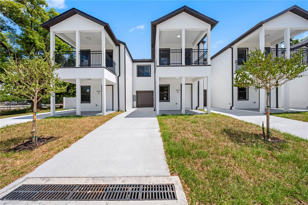 A row of three modern, white two-story townhouses with covered balconies and concrete driveways — 7015 N CENTRAL AVENUE Unit B, TAMPA, FL