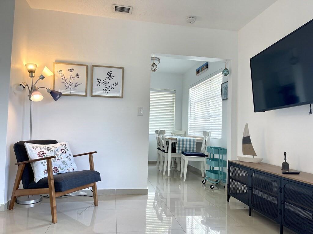 A living room with a dark armchair, floor lamp, wall art, and a dining area — 29 NE 3rd Street # A, Dania Beach FL 33004, DANIA BEACH, FL