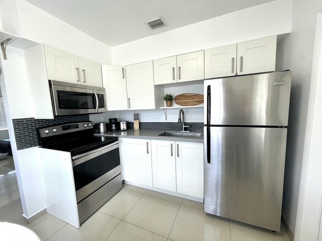 A kitchen with white cabinets, stainless steel appliances, and a dark gray tiled backsplash — 29 NE 3rd Street # A, Dania Beach FL 33004, DANIA BEACH, FL