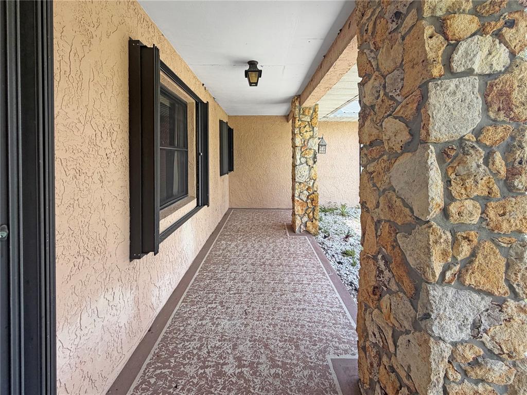 A covered outdoor walkway features stucco walls, stone pillars, and a patterned concrete floor — 2417 TRAVELERS PALM DRIVE, EDGEWATER, FL