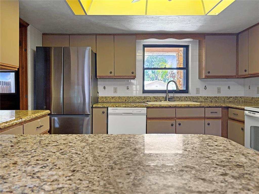 A kitchen features granite countertops, tan cabinets, a stainless steel refrigerator, and a white dishwasher — 2417 TRAVELERS PALM DRIVE, EDGEWATER, FL