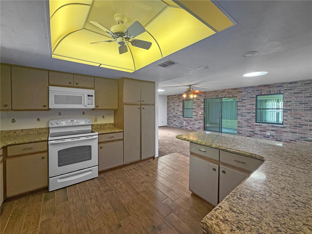 A kitchen with granite countertops and brown cabinets opens to a brick-walled living area — 2417 TRAVELERS PALM DRIVE, EDGEWATER, FL