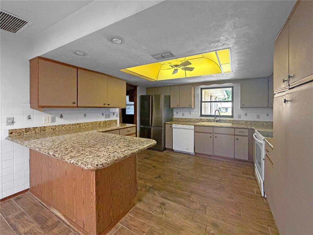 A kitchen features wood cabinets, granite countertops, a stainless steel refrigerator, and a yellow light fixture — 2417 TRAVELERS PALM DRIVE, EDGEWATER, FL