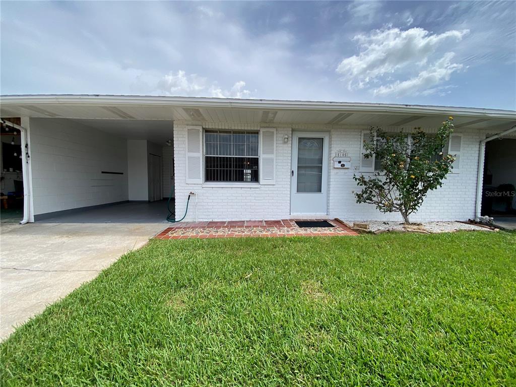A white brick house features a carport, a front door, and a small tree — 5105 ROSE PLACE N, PINELLAS PARK, FL