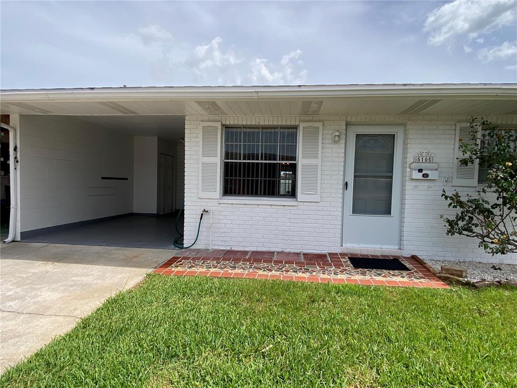 A white brick house exterior features a carport, a front door, and a tiled porch — 5105 ROSE PLACE N, PINELLAS PARK, FL