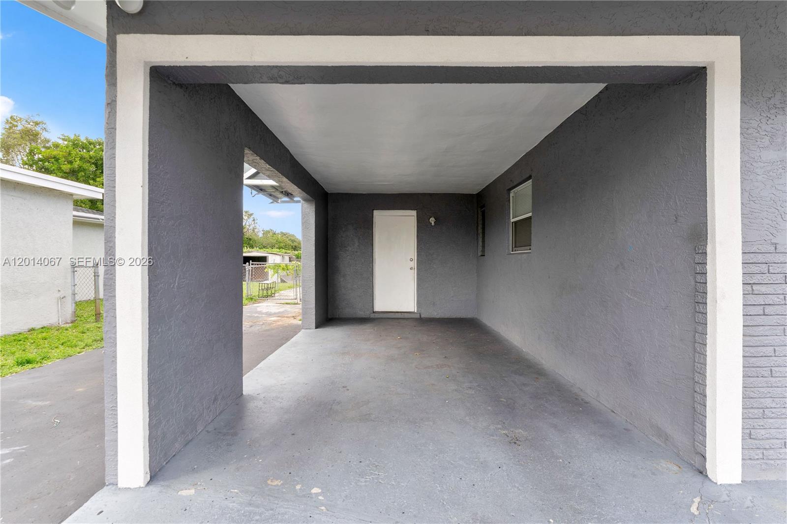 A covered carport features gray stucco walls, a concrete floor, and a white entry door — 3171 NW 16th St, Lauderhill FL 33311, LAUDERHILL, FL
