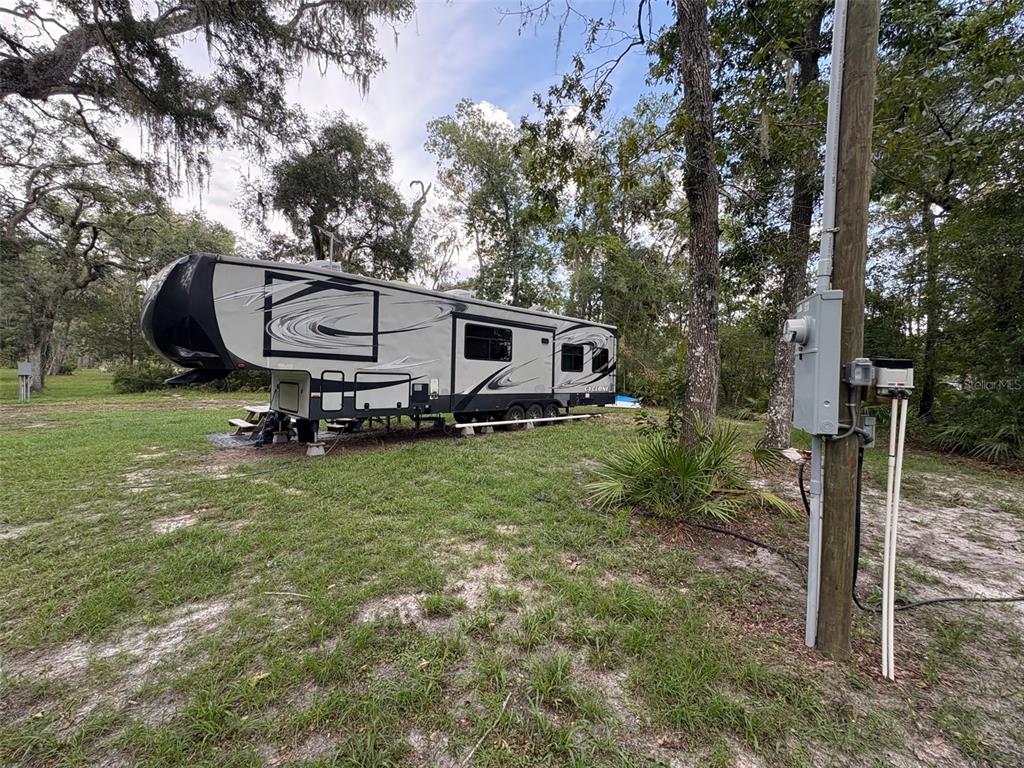 A large fifth-wheel RV is parked on a grassy lot next to a utility pole — 1525 NE 930TH STREET, OLD TOWN, FL
