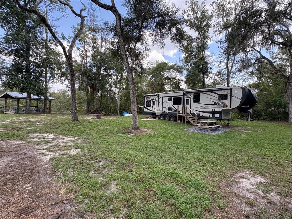 A large fifth-wheel RV is parked on a grassy lot near a wooden pavilion — 1525 NE 930TH STREET, OLD TOWN, FL
