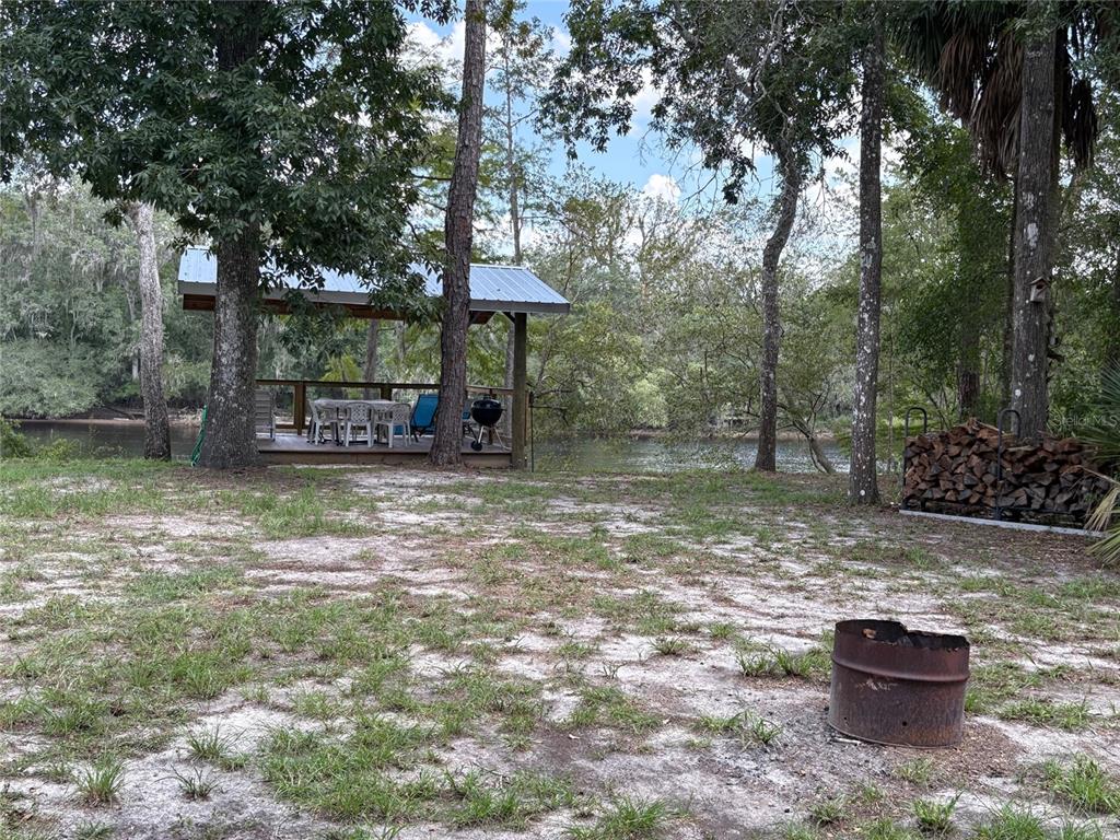 A backyard features a fire pit, a wood rack, and a covered deck overlooking a river — 1525 NE 930TH STREET, OLD TOWN, FL