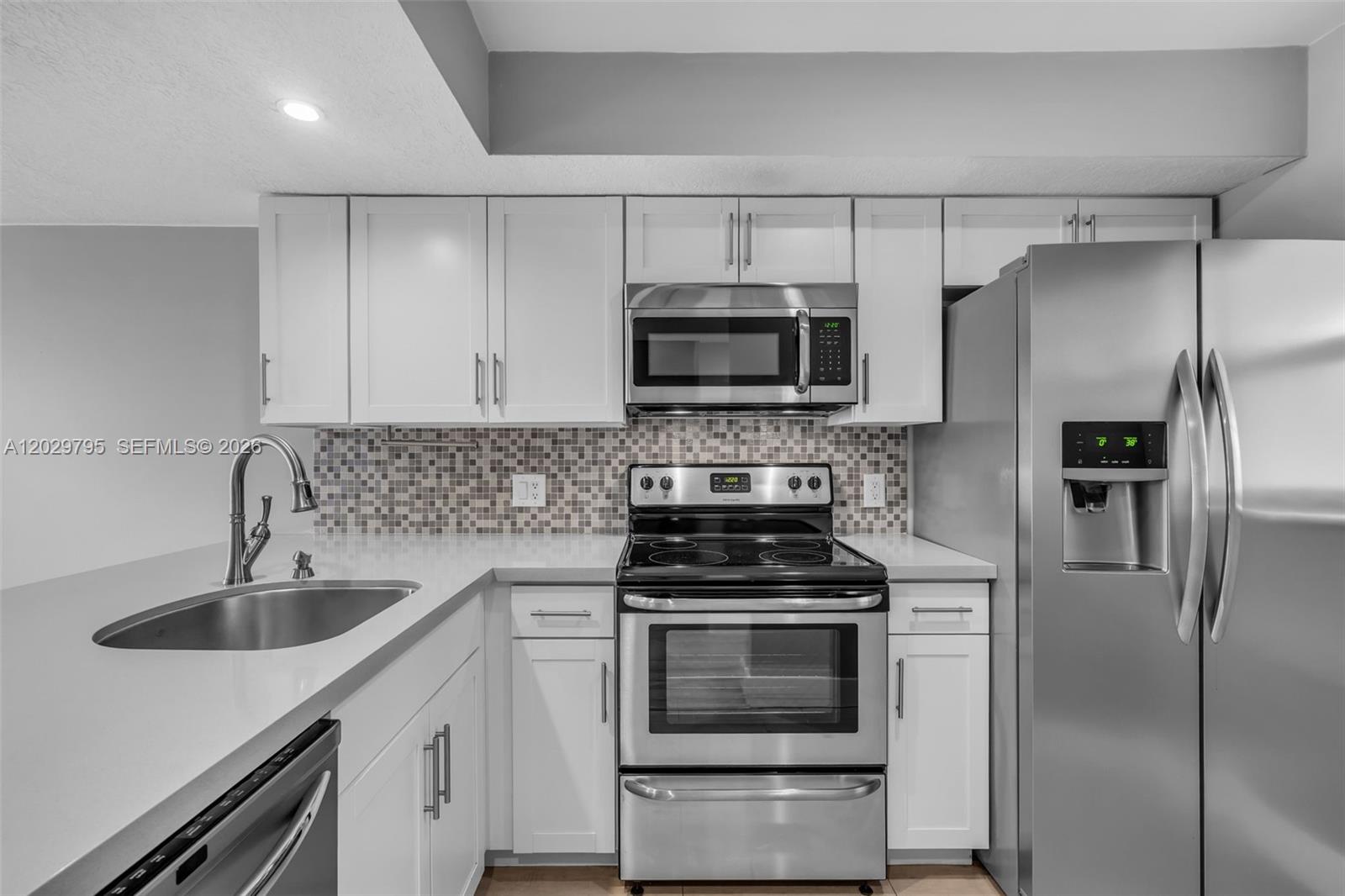 A kitchen features white cabinets, stainless steel appliances, and a mosaic tile backsplash — 4600 SW 67th Ave # 264, Miami FL 33155, MIAMI, FL