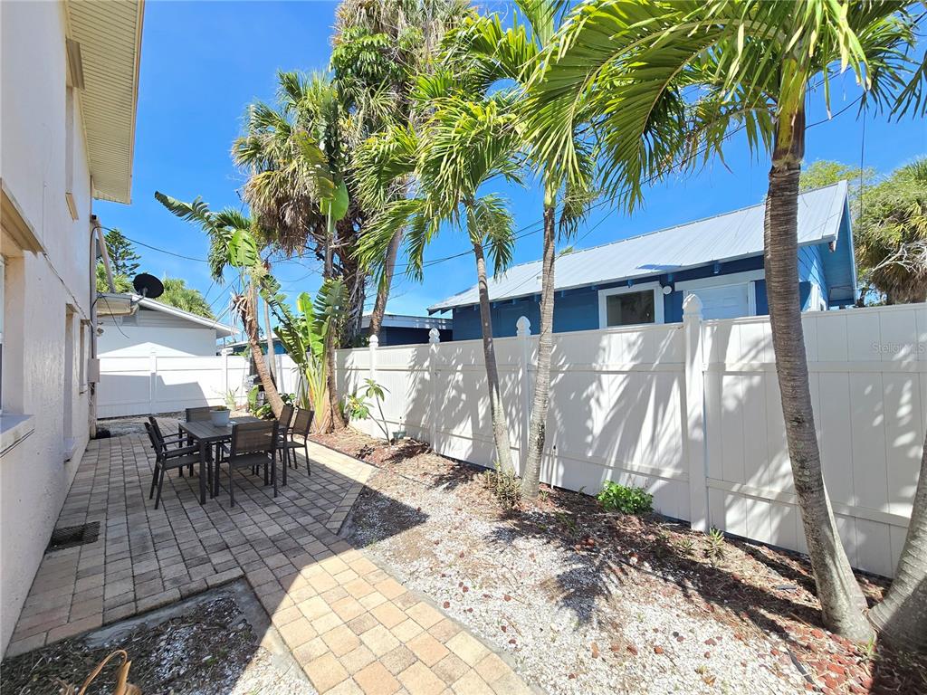 A paved patio area features a dining set beside a white vinyl fence and palms — 525 73RD AVENUE UNIT 2, ST PETE BEACH, FL