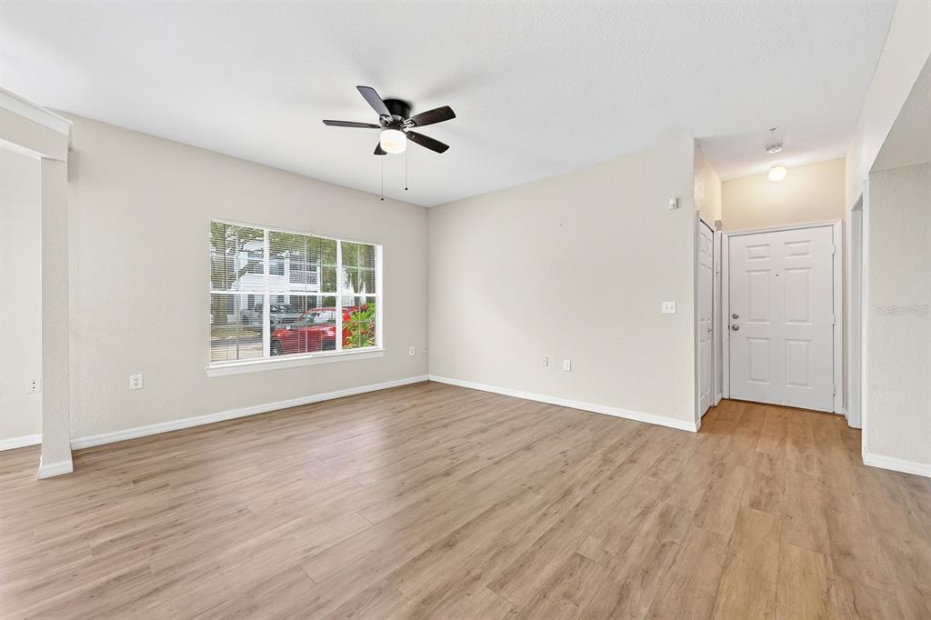 An empty living room with light-colored walls, wood-look flooring, a ceiling fan, and an entryway — 5118 CITY STREET UNIT 514, ORLANDO, FL