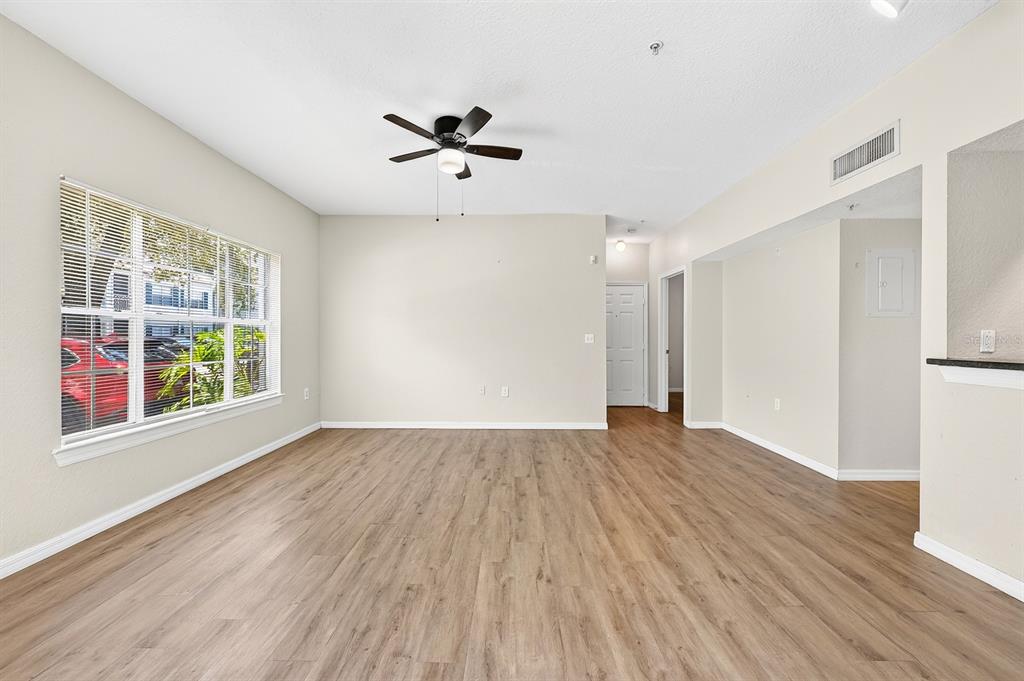 An empty living room features light wood-look flooring, a ceiling fan, and a large window — 5118 CITY STREET UNIT 514, ORLANDO, FL