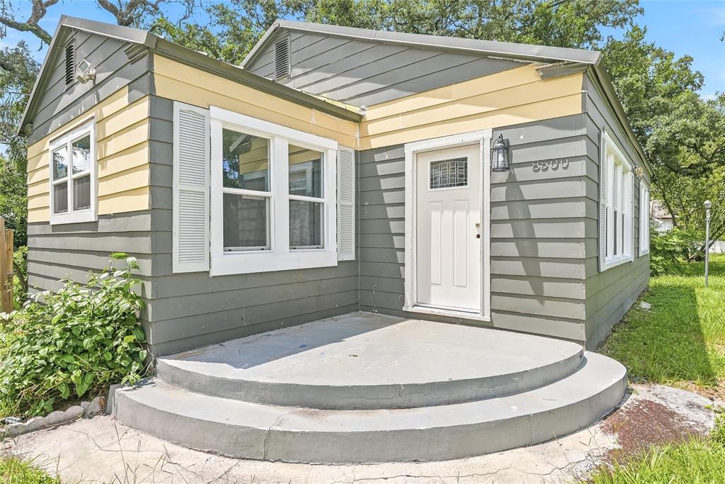 A small house exterior features gray and yellow horizontal siding, a white door, and concrete steps — 8500 N BOULEVARD, TAMPA, FL