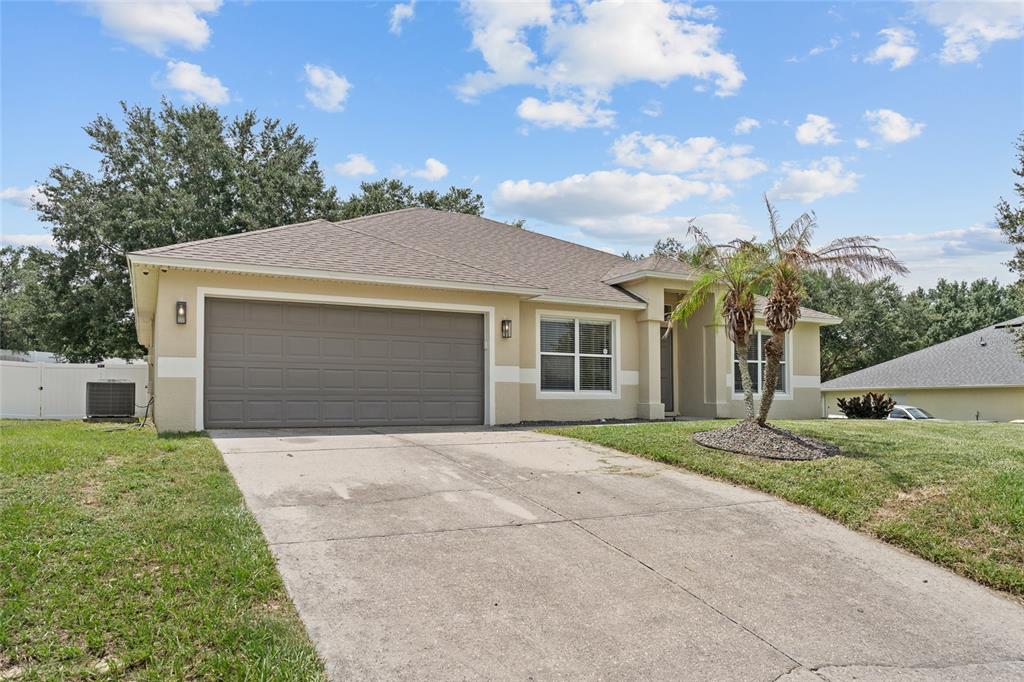 A single-story house with a beige stucco exterior, a two-car garage, and a concrete driveway — 1128 LAKEVIEW OAKS DRIVE, MINNEOLA, FL