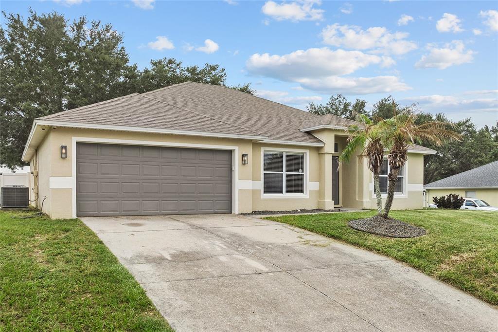 A single-story house with a beige exterior, a two-car garage, and a concrete driveway — 1128 LAKEVIEW OAKS DRIVE, MINNEOLA, FL