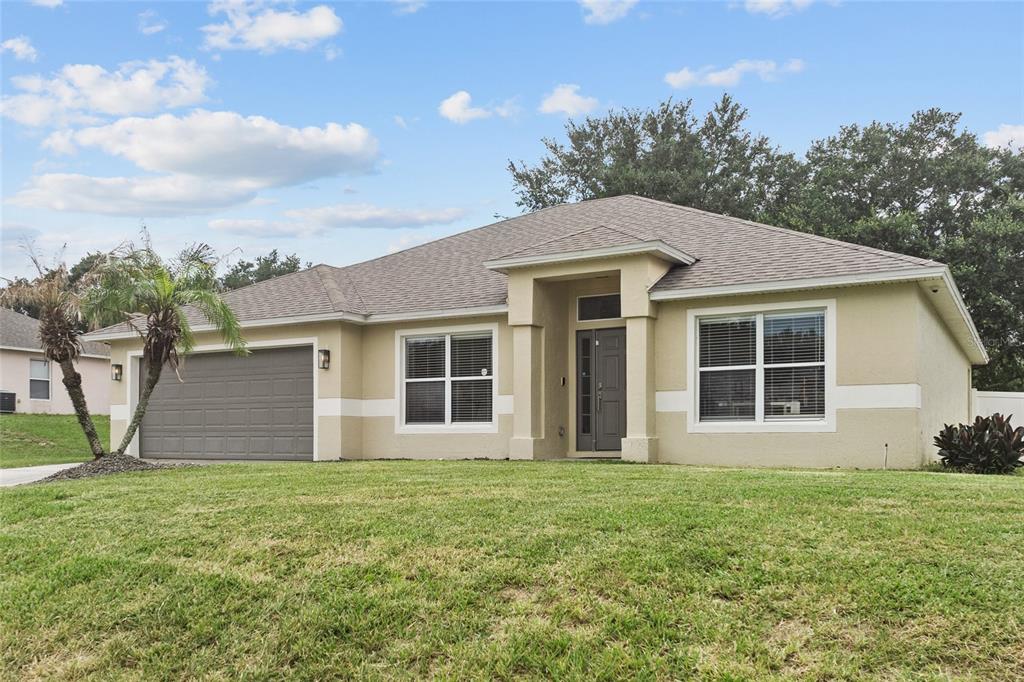 A single-story house with a tan stucco exterior, a gray garage door, and a front entrance — 1128 LAKEVIEW OAKS DRIVE, MINNEOLA, FL