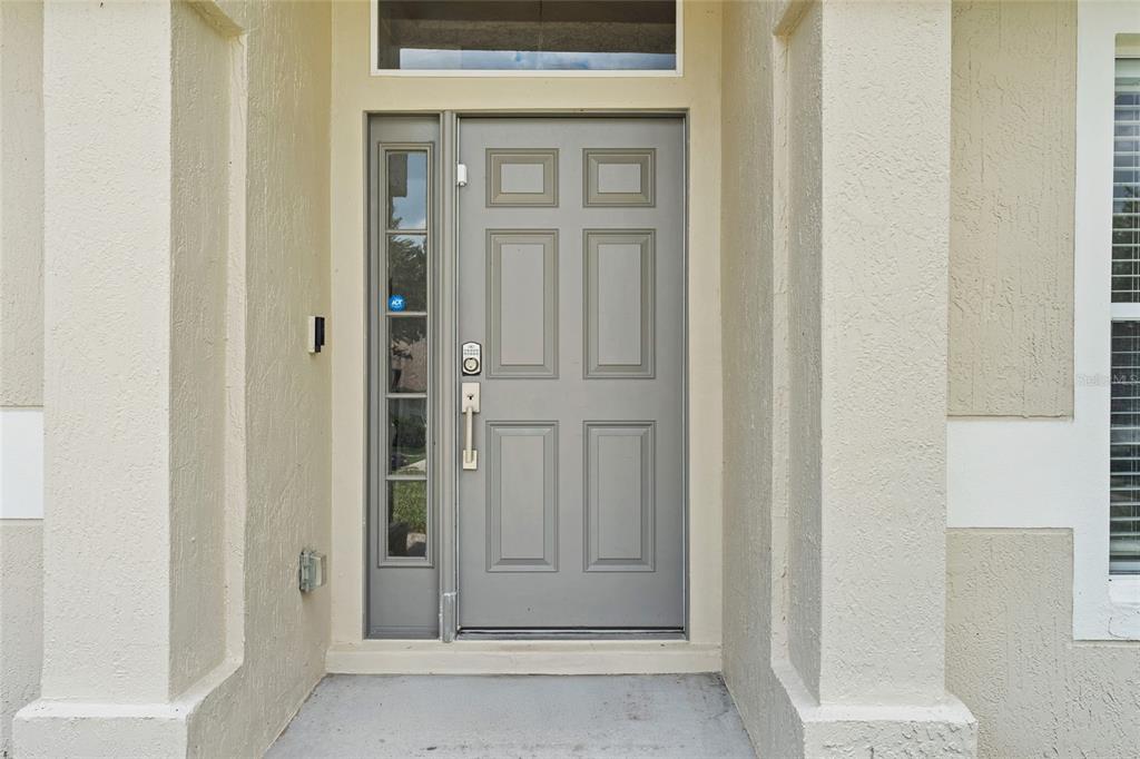 A gray front door with a side window and a transom window under a covered entryway — 1128 LAKEVIEW OAKS DRIVE, MINNEOLA, FL