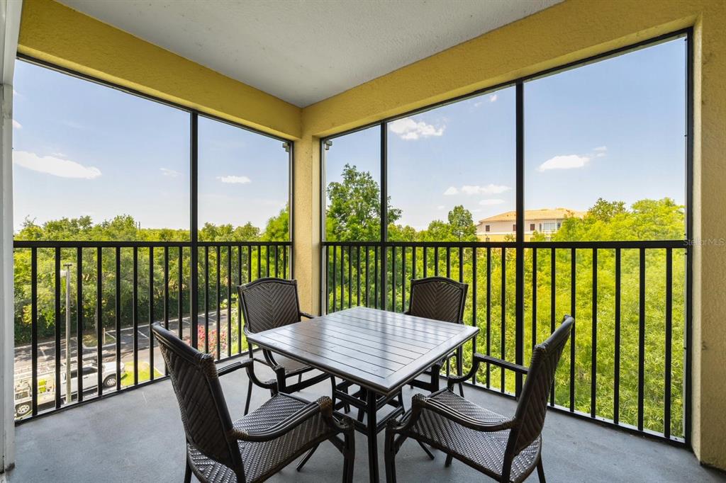 A screened-in balcony features a dining table with four chairs overlooking trees and a parking lot — 8763 WORLDQUEST BOULEVARD UNIT 5406, ORLANDO, FL