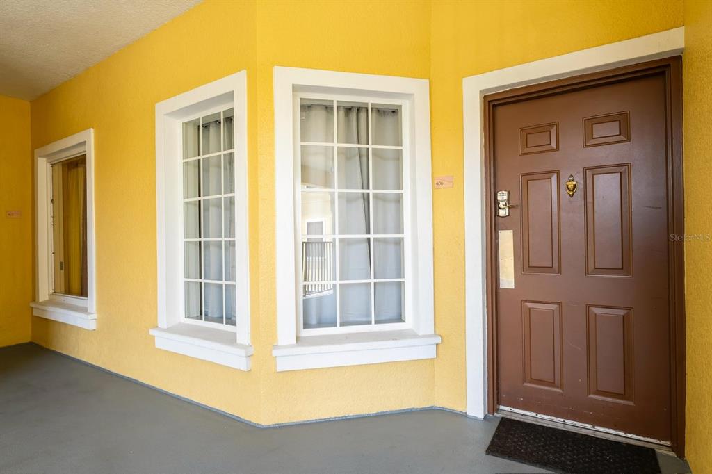 A brown front door sits next to two white-framed windows on a yellow exterior wall — 8763 WORLDQUEST BOULEVARD UNIT 5406, ORLANDO, FL