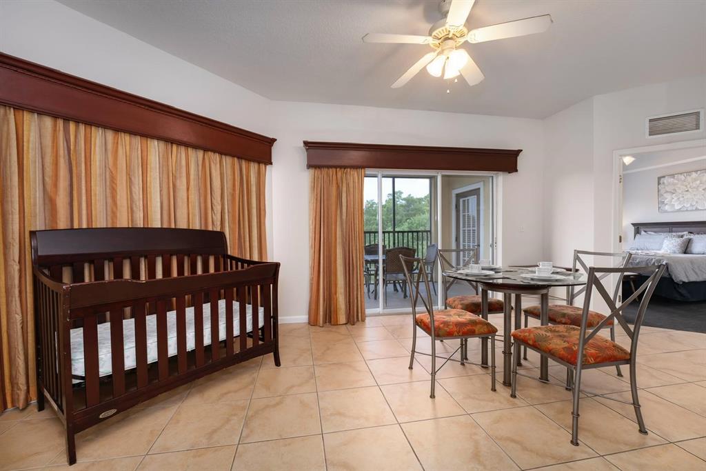 A room with tile floors, a crib, a dining set, and a sliding glass door — 8763 WORLDQUEST BOULEVARD UNIT 5406, ORLANDO, FL