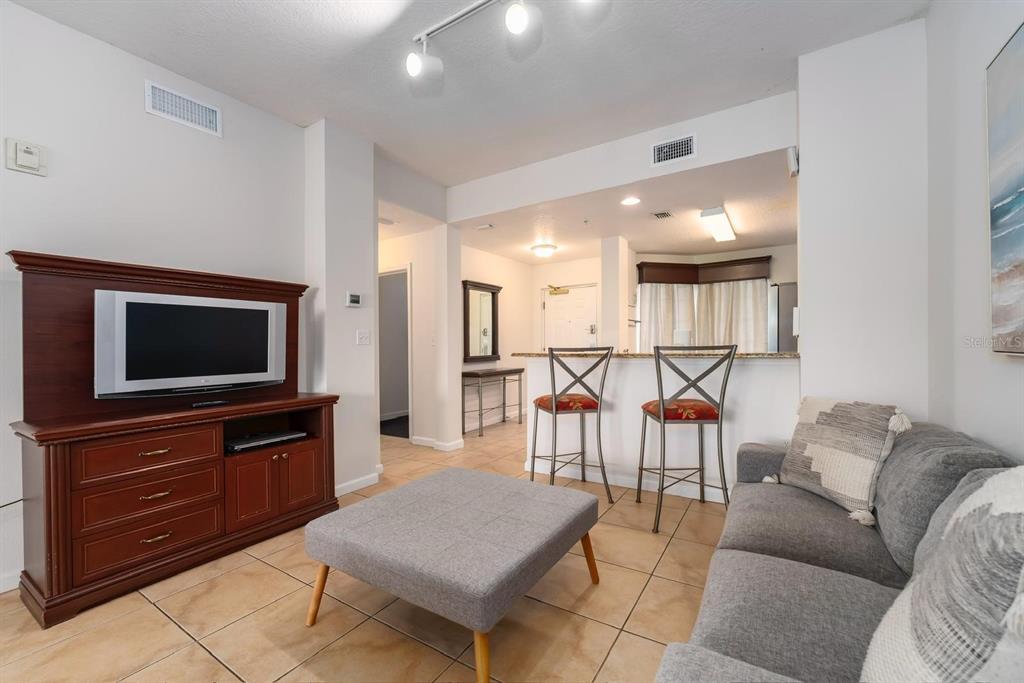 A living room features a television console, gray sofa, ottoman, and a breakfast bar area — 8763 WORLDQUEST BOULEVARD UNIT 5406, ORLANDO, FL