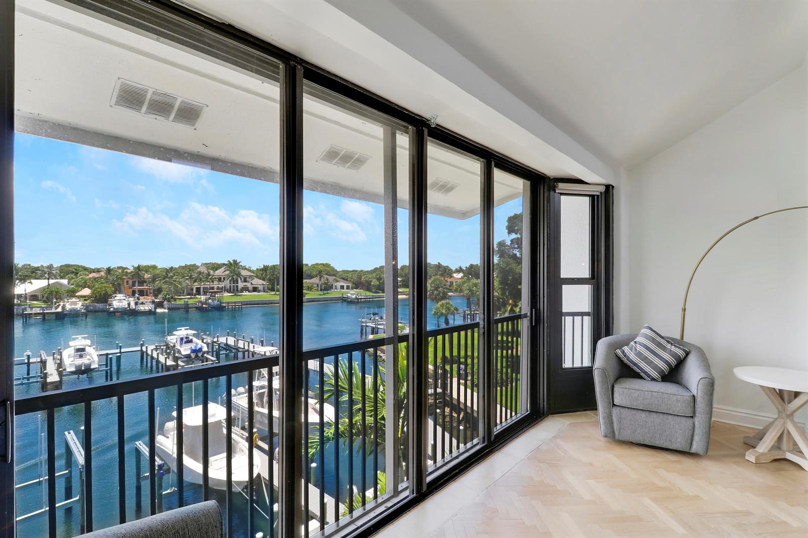 A room with herringbone wood floors and a balcony overlooking a canal with docked boats — 543 Bay Colony Drive N Slip 8, Juno Beach FL 33408, JUNO BEACH, FL
