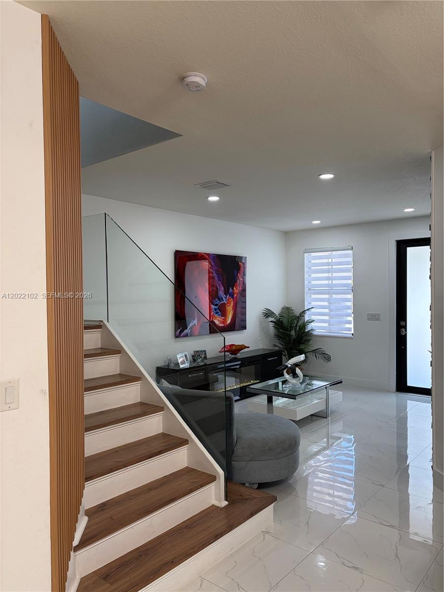 A modern living room features a glass-railed staircase, wood-tread steps, and white tile flooring — 3409 W 92nd Pl, Hialeah FL 33018, HIALEAH, FL