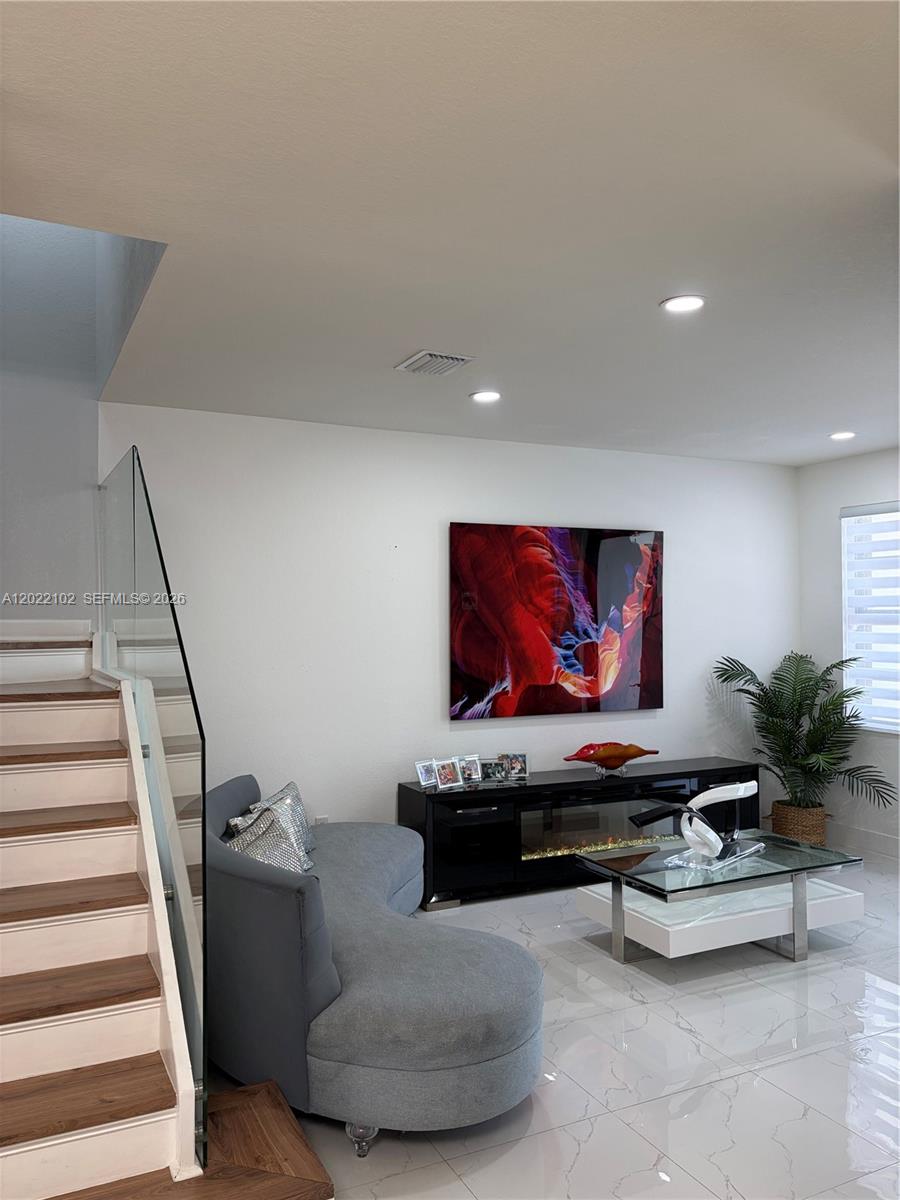 A modern living room features a curved gray sofa, glass coffee table, and staircase — 3409 W 92nd Pl, Hialeah FL 33018, HIALEAH, FL