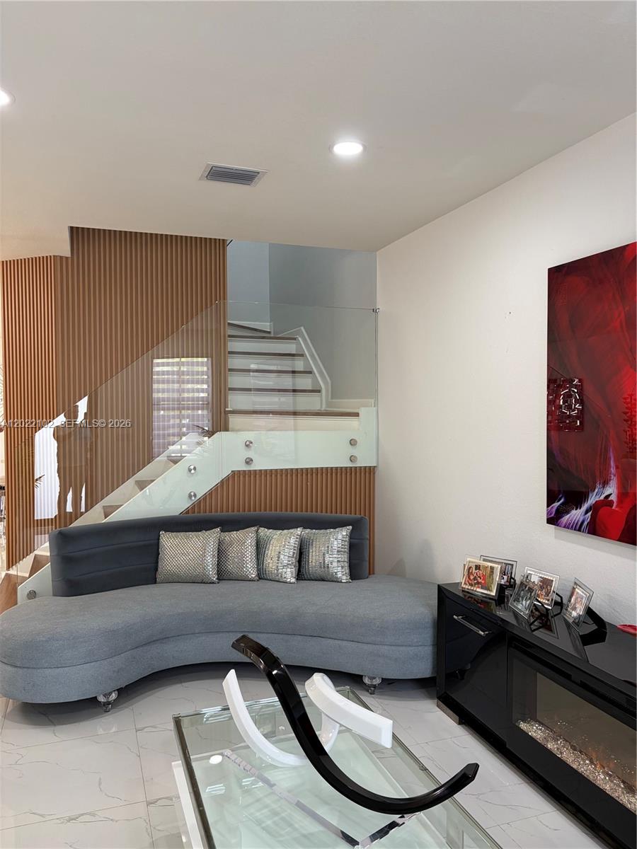 A living room features a curved gray sofa, glass staircase railing, and wood-slat wall paneling — 3409 W 92nd Pl, Hialeah FL 33018, HIALEAH, FL