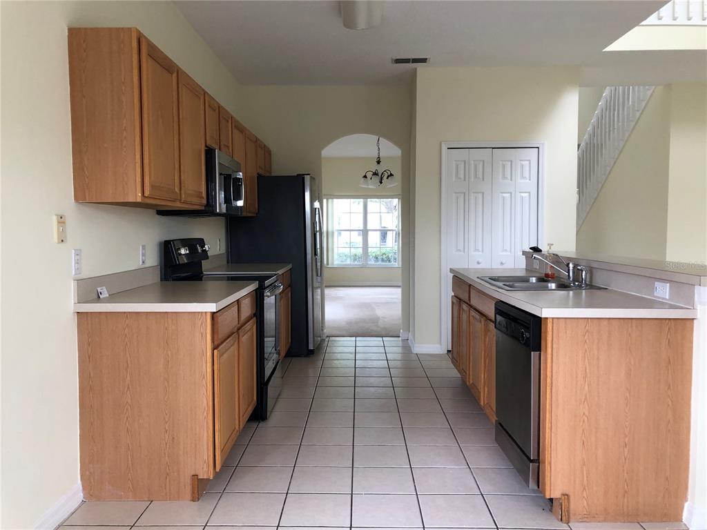 A kitchen with light wood cabinets, black appliances, and tile flooring leads to a dining area — 638 KENSINGTON DRIVE, DAVENPORT, FL