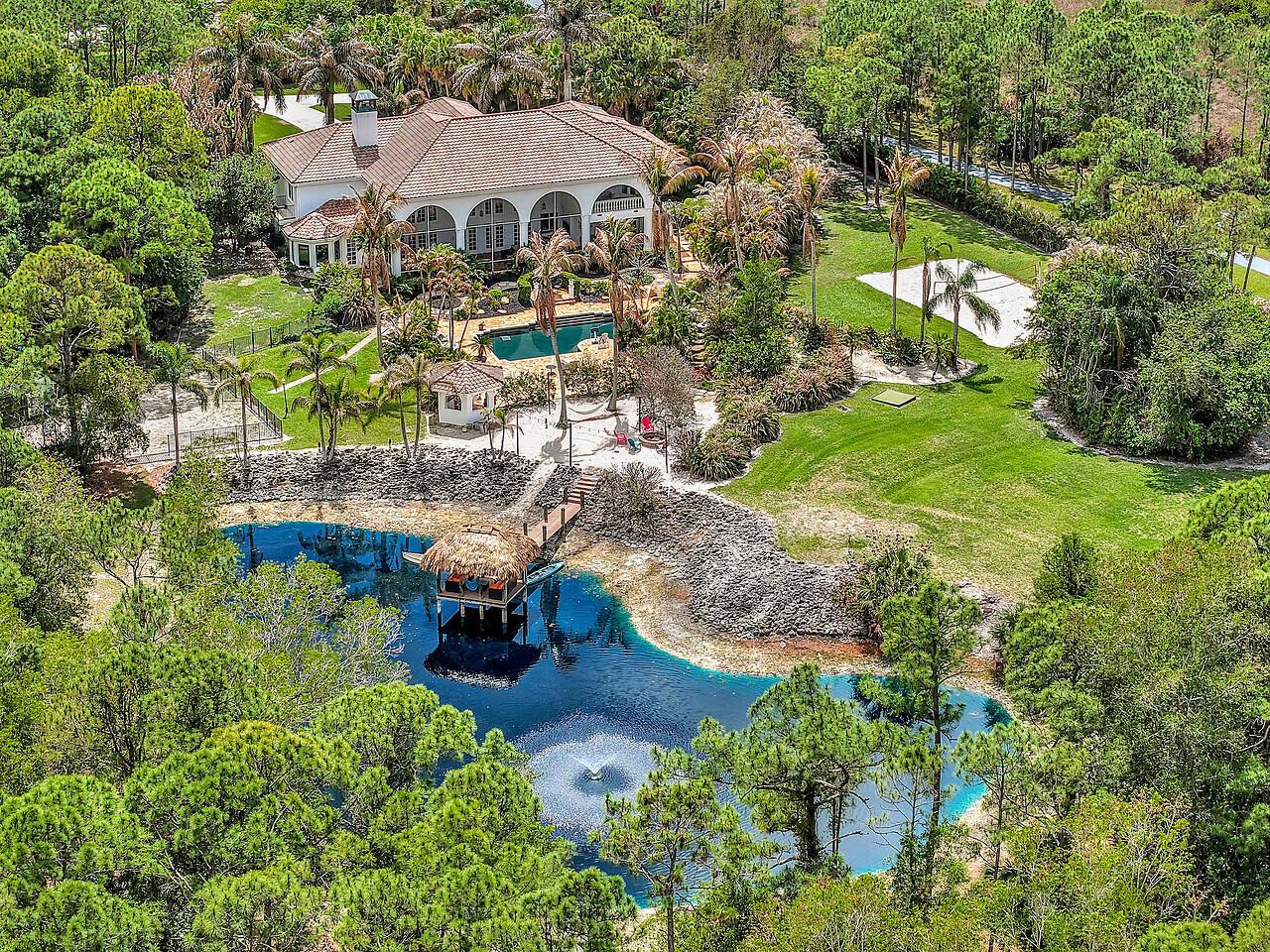 An aerial view of a house with a pool, a pond, and a tiki hut — 2584 SE Ranch Acres Circle, Jupiter FL 33478, JUPITER, FL