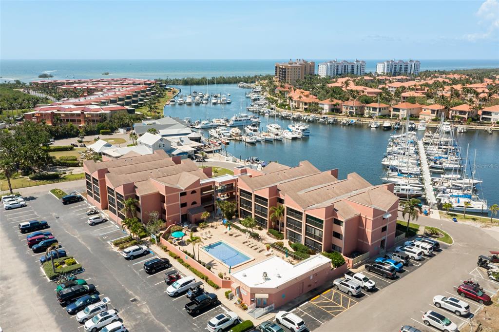 An aerial view shows a multi-story pink apartment complex with a pool and marina — 3160 MATECUMBE KEY ROAD UNIT 233, PUNTA GORDA, FL
