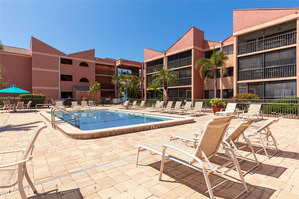 A rectangular swimming pool sits on a paved patio surrounded by multi-story residential buildings — 3160 MATECUMBE KEY ROAD UNIT 233, PUNTA GORDA, FL