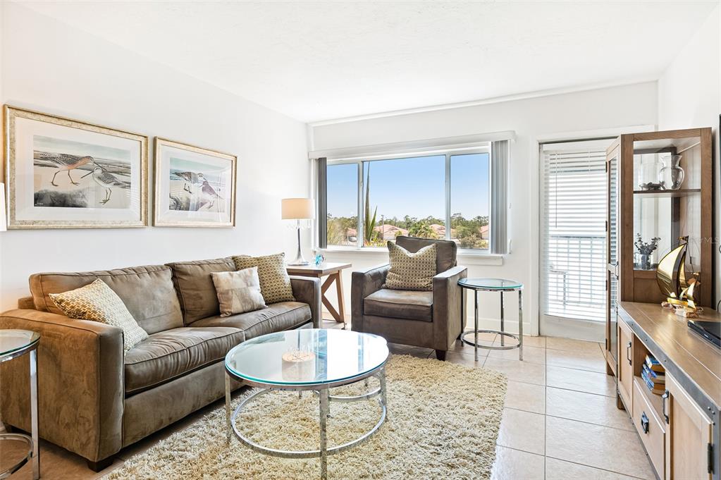 A living room features a brown sofa, armchair, glass coffee table, and a large window — 3160 MATECUMBE KEY ROAD UNIT 233, PUNTA GORDA, FL