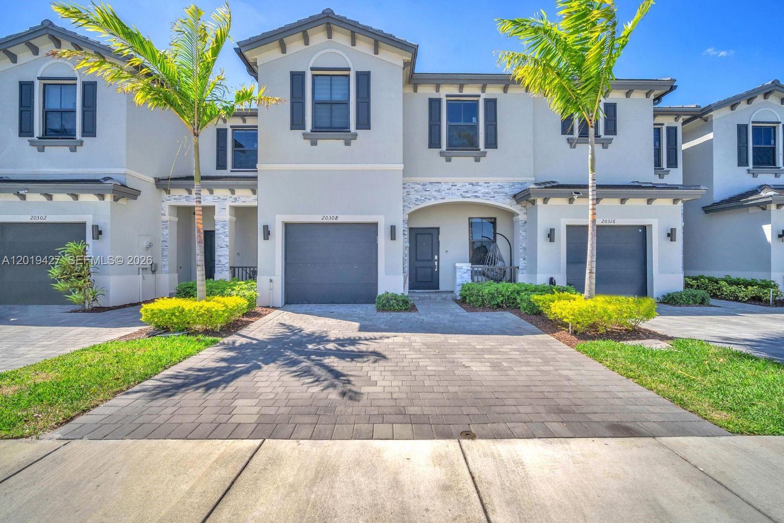 A two-story townhouse features a gray garage, a paved driveway, and palm trees — 20308 NW 6th Pl, Miami Gardens FL 33169, MIAMI GARDENS, FL