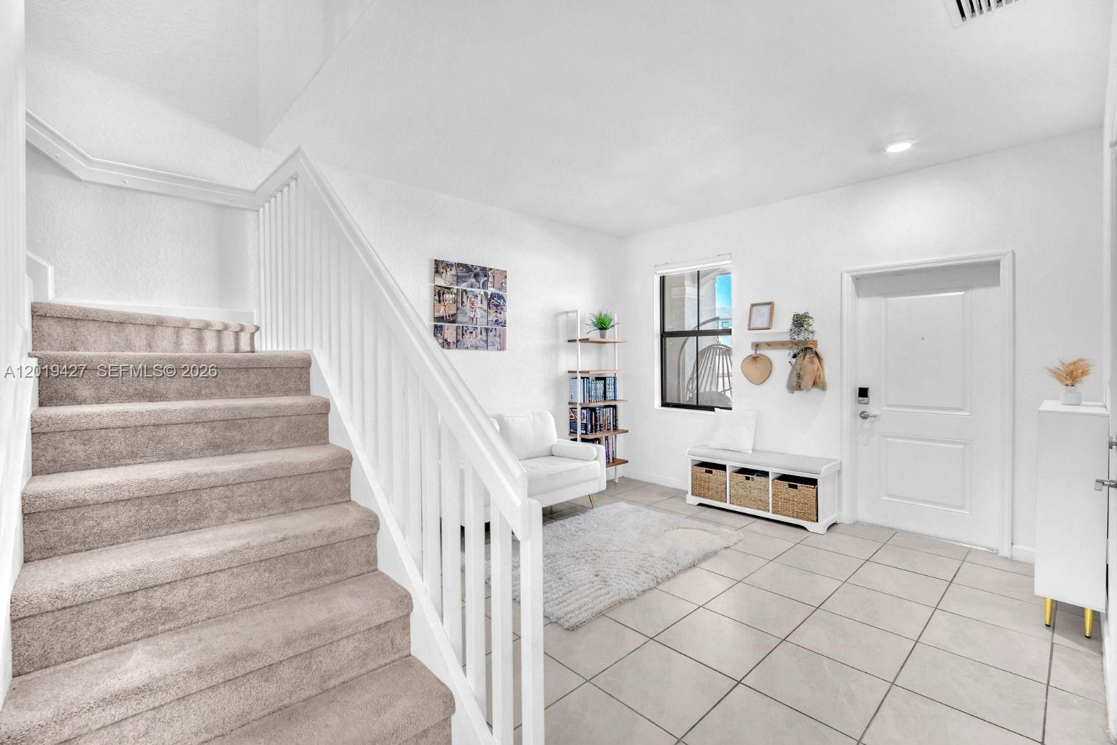A bright entryway features a carpeted staircase, tiled flooring, a white bench, and a chair — 20308 NW 6th Pl, Miami Gardens FL 33169, MIAMI GARDENS, FL